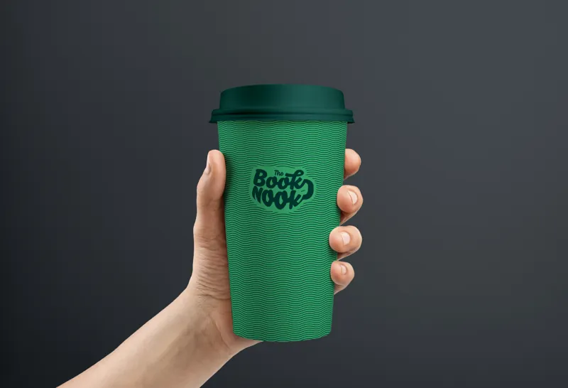A hand holding a green reusable cup printed with the Book Nook logo.