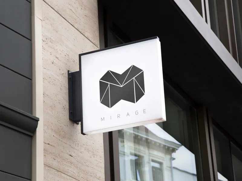 A square hanging sign on a stone building, showing a faceted black M with Mirage spaced out beneath it.